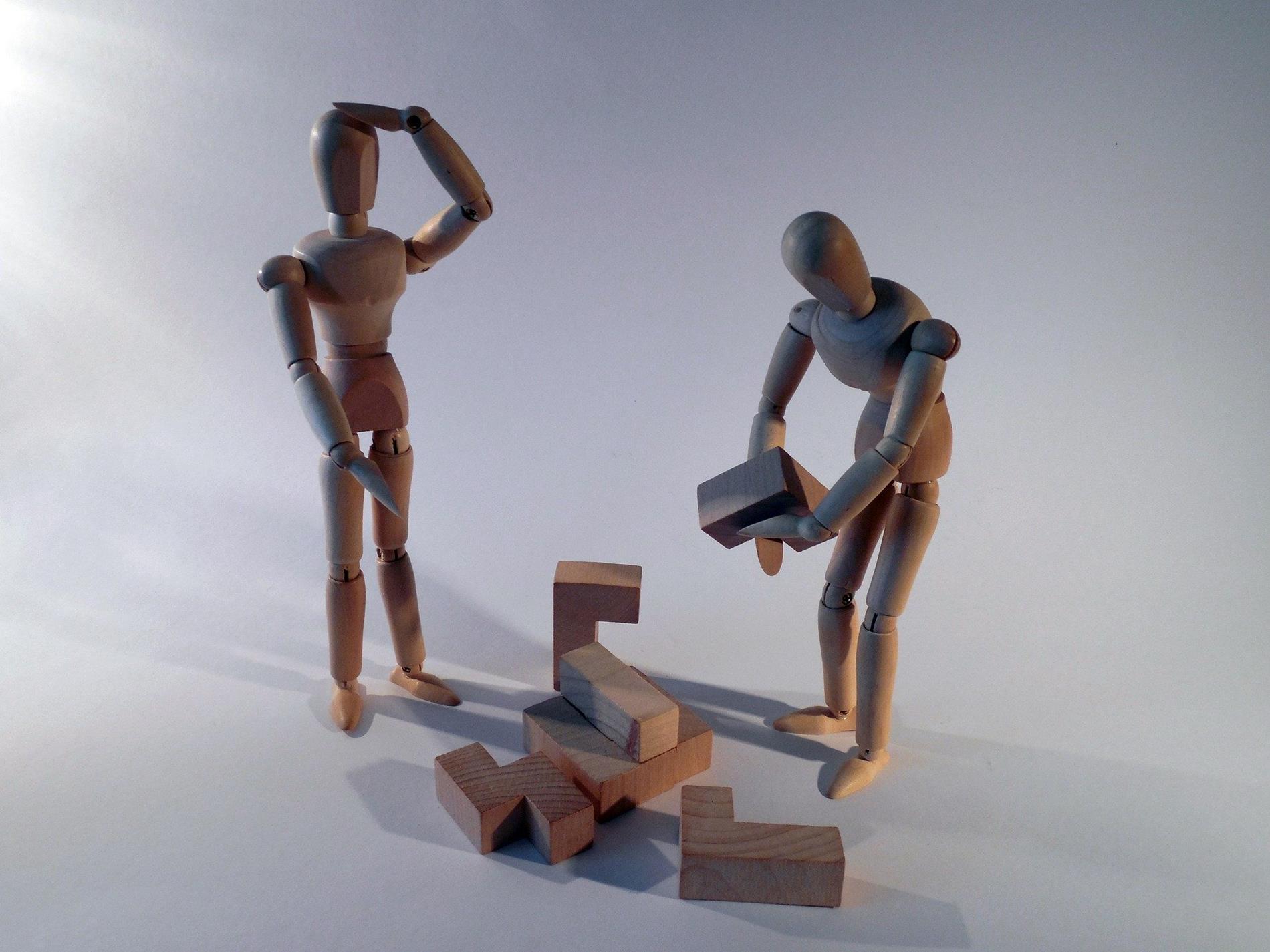wooden human figures trying to solve a wooden puzzle