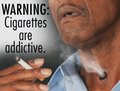 Man smoking with sign warning cigarettes are addictive