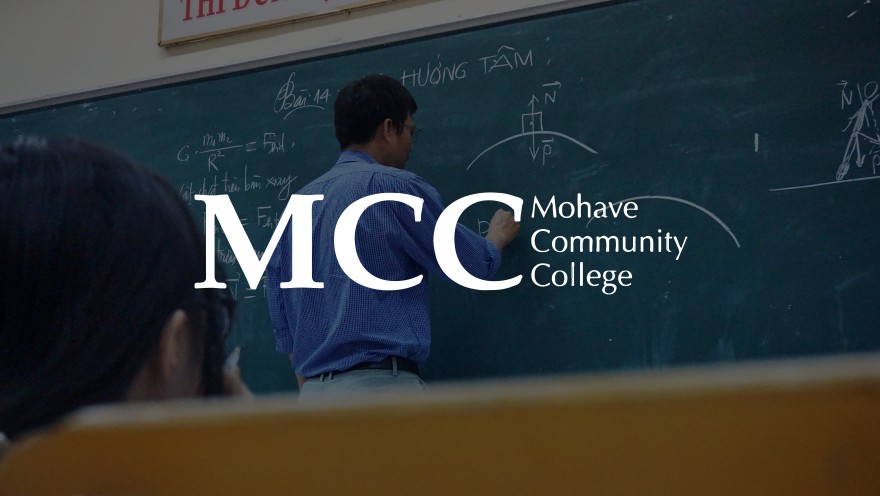 MCC logo with a teacher in the background writing on a chalk board teaching a class