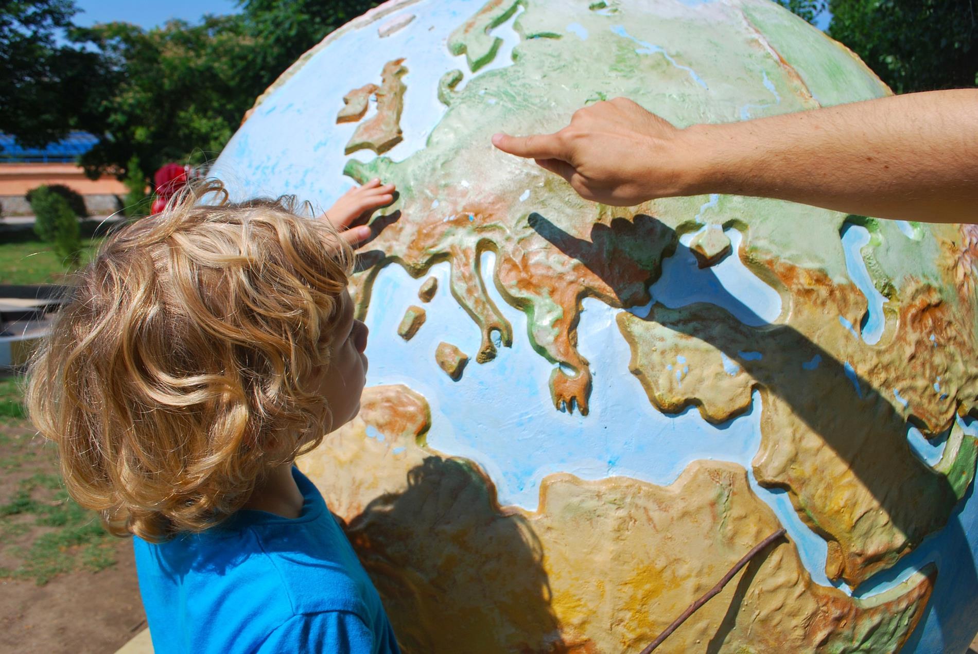 small child touching large globe with adult hand pointing finger at globe