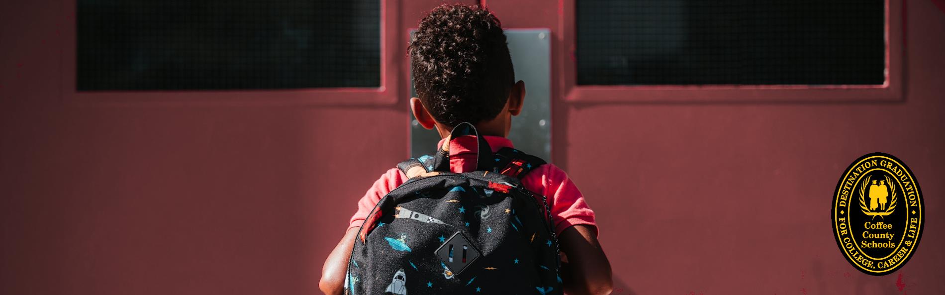 Boy with backpack standing at school doors