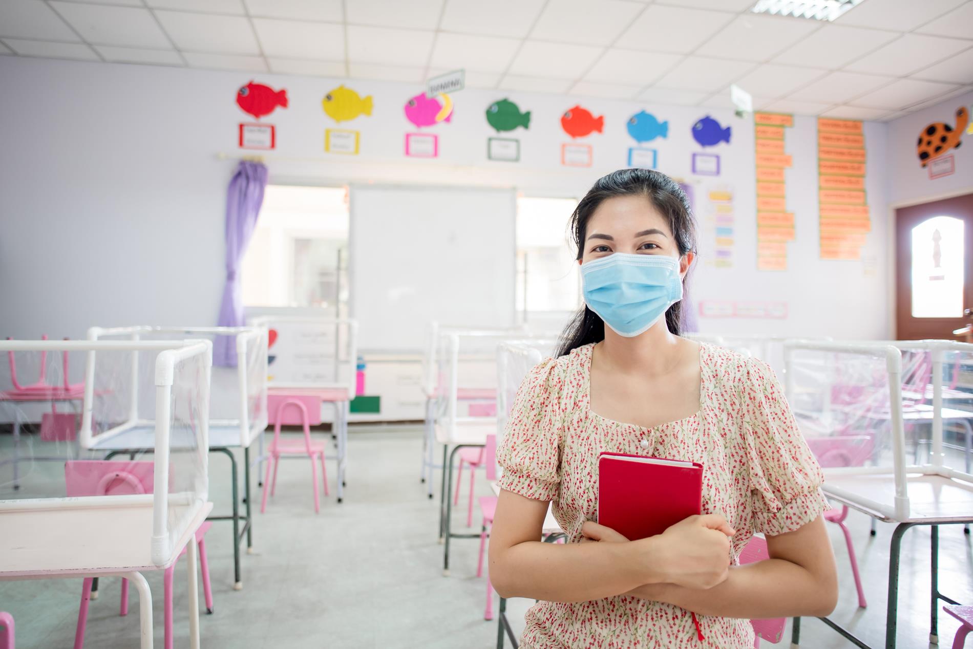 School teacher in her classroom, wearing a mask.
