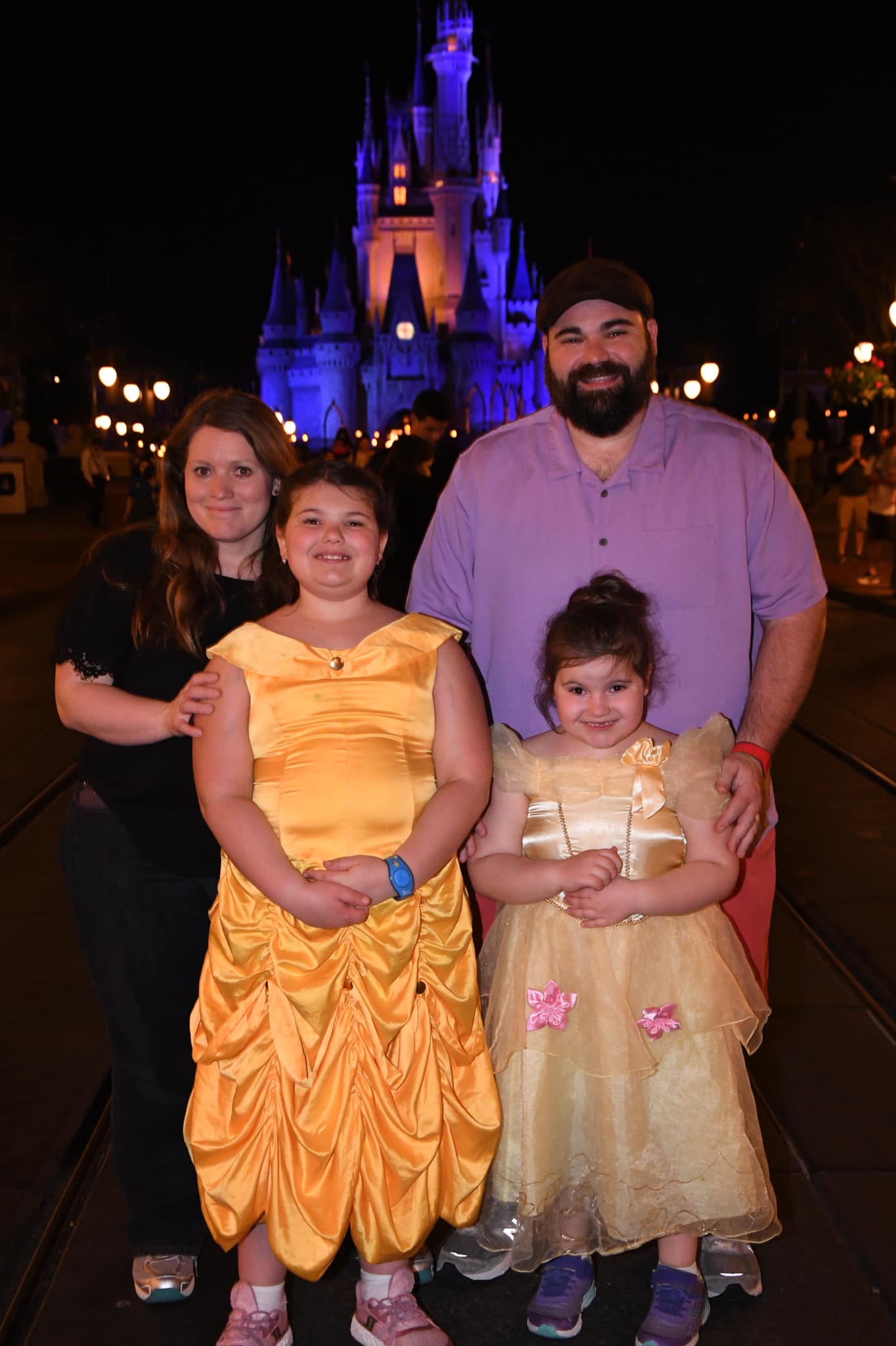 Family photo - Man, woman, two young daughters standing in front of Cinderella's castle at night
