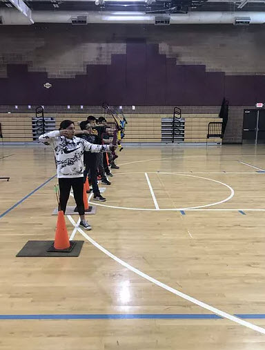 students in gym shooting bow and arrows