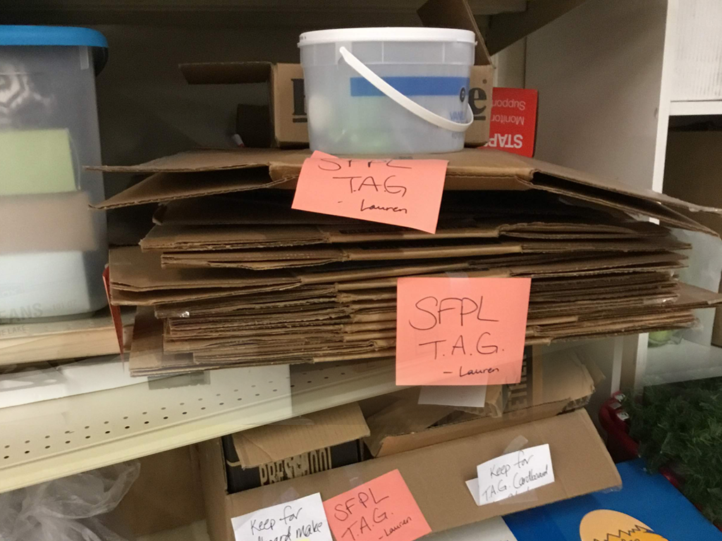 Stacks of flatten cardboard boxes and other materials labeled "SFPL Teen" on storage shelves