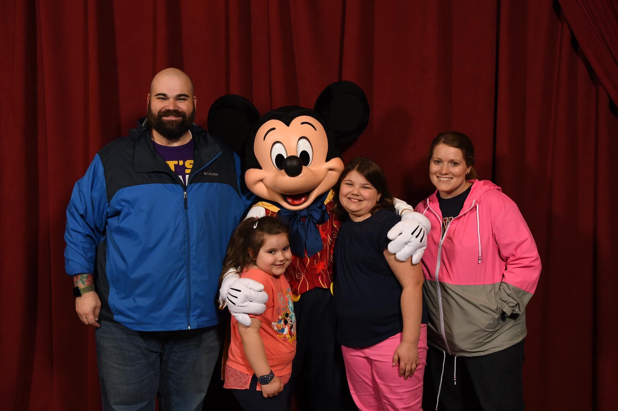 Family photo - Man, woman, two young daughters standing with Mickey Mouse