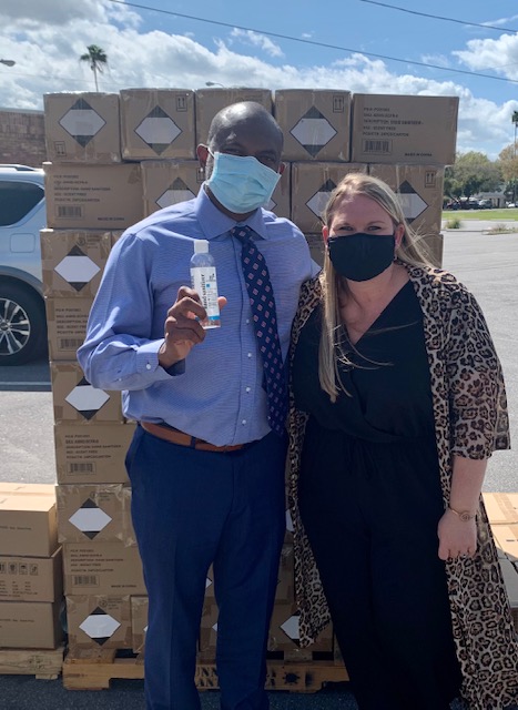 Mrs. Rose and Mr. Smith standing in front of the Advent Health hand sanitizer donation.