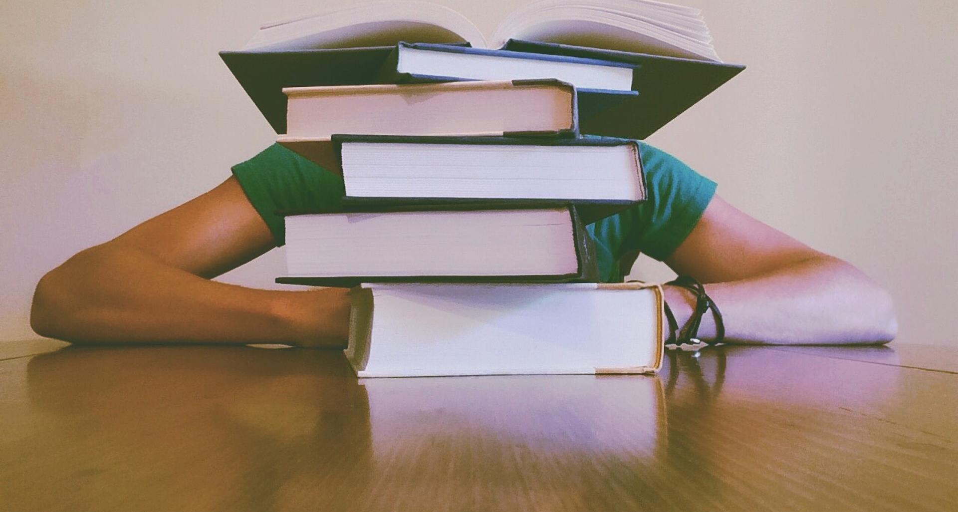 photograph of a view of a person being blocked by a stack of books on a table 