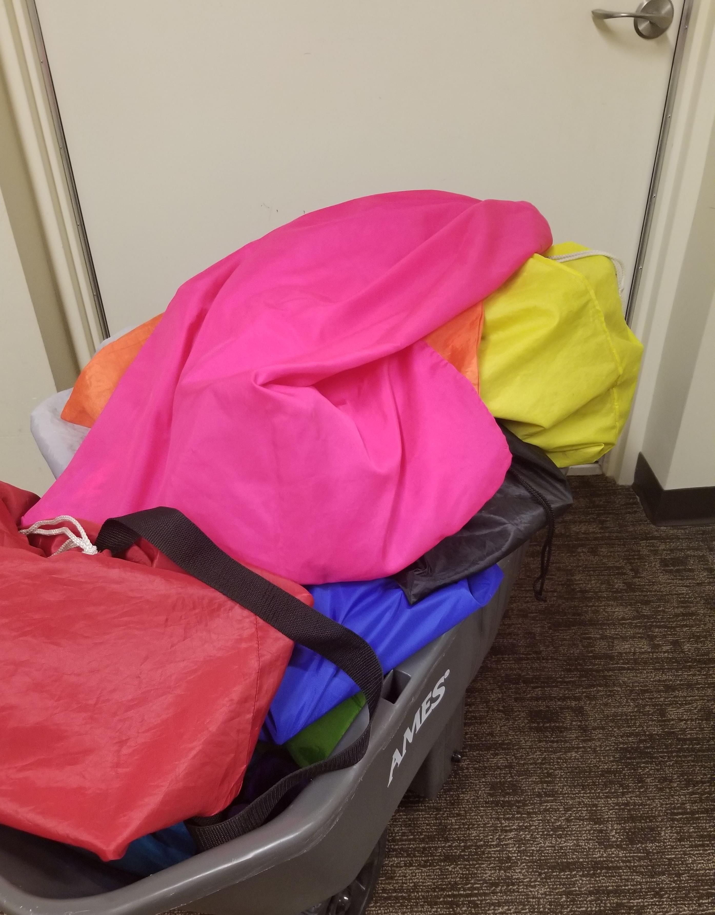 gray cart heaped with brightly colored cargo bags parked in front of a an exit door.